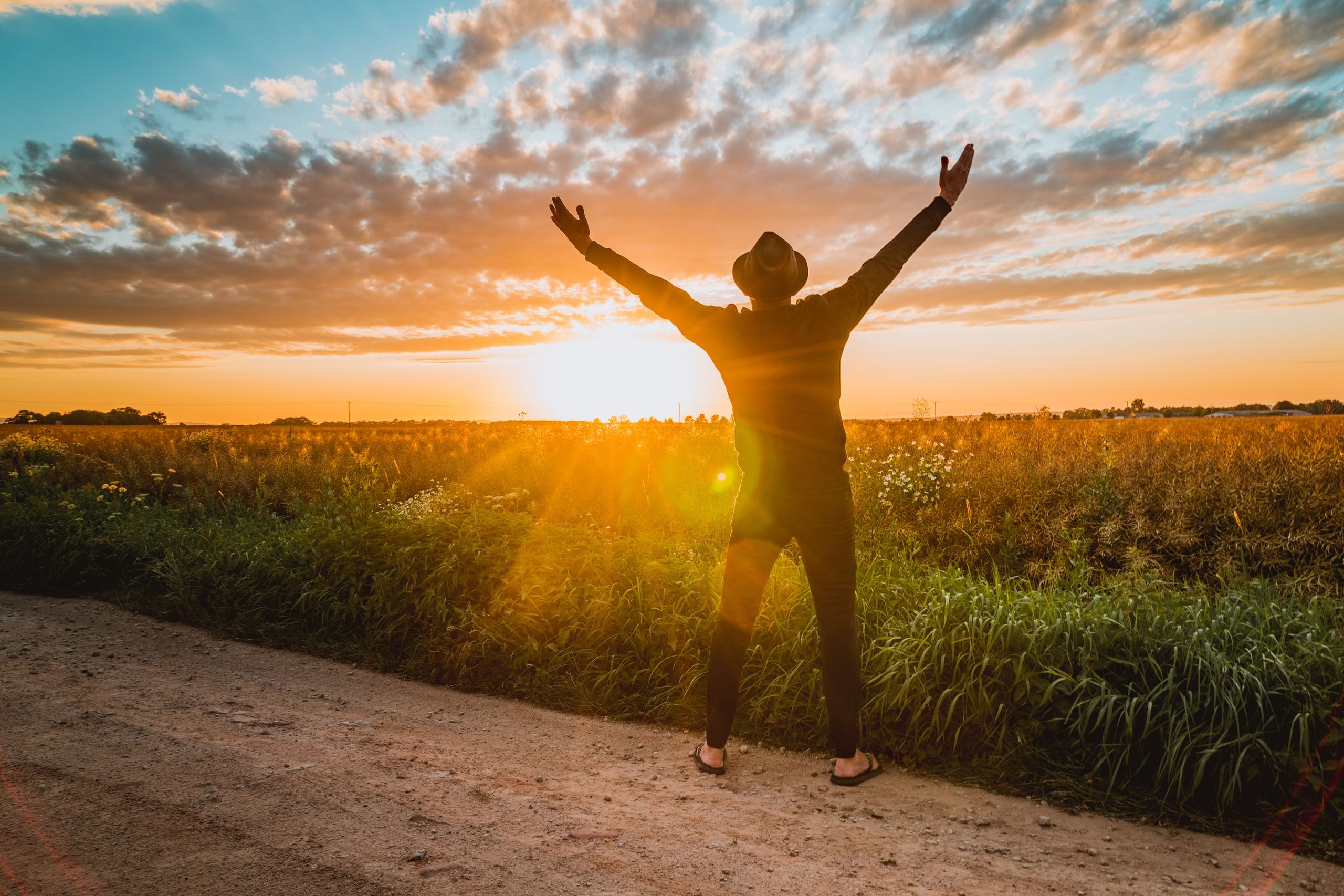 Photo by Peggy Anke - Racing Fans A man raises arms in freedom at sunrise in a rural field, expressing joy and connection with nature.