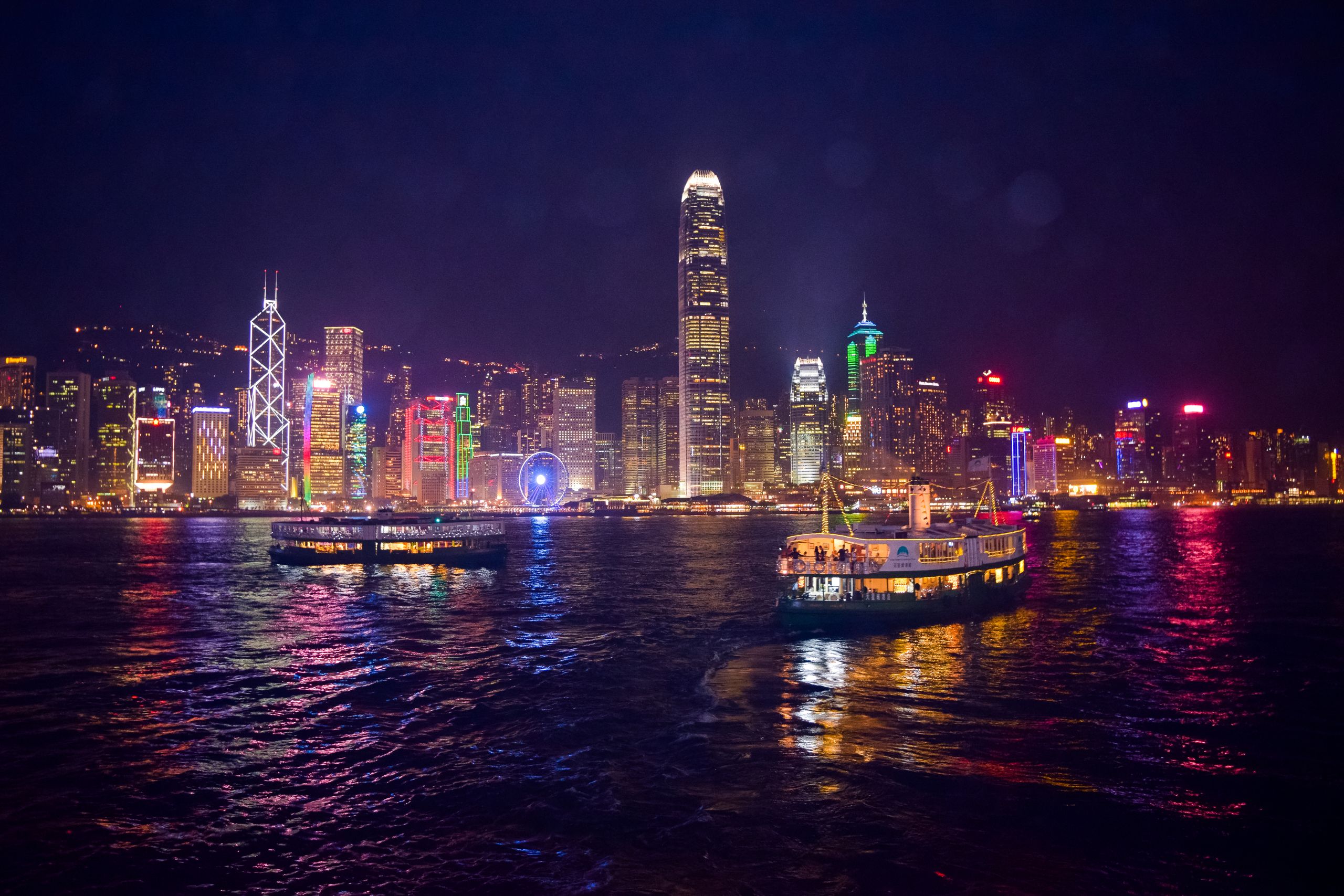 Photo by Julian Lobo - Racing Fans Captivating night view of Hong Kong's illuminated skyline and ferries reflecting on the water.