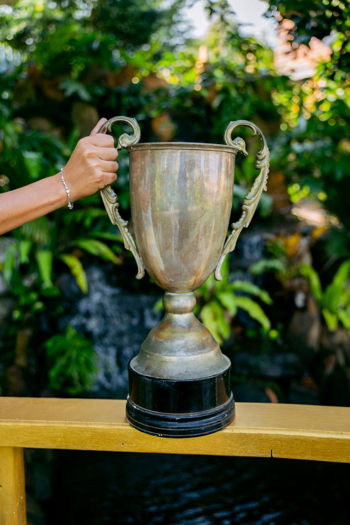 Close-up of a hand holding a large trophy in an outdoor garden setting.